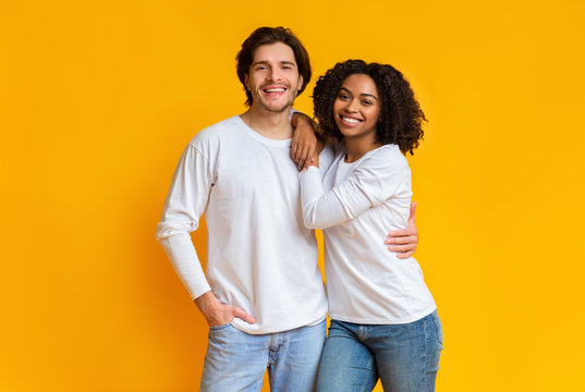 Portrait of smiling mixed-race couple posing over yellow background in studio