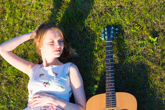 Beautiful hippie girl with guitar lying on grass