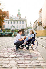 Young Couple In love, pretty woman in wheelchair walking In The old City center. Couple in love in the city center.