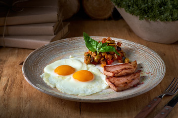 plate of fried eggs with bacon and vegetables on wooden table. English breakfast on table