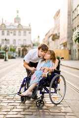 Happy couple with disabled woman walking at old city background. Relationship concept within disability issues with woman on wheelchair and young handsome husband