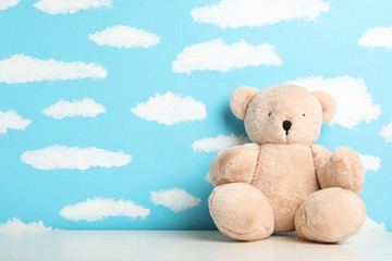 Teddy bear on white table near wall with painted blue sky, space for text. Baby room interior