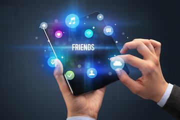 Businessman holding a foldable smartphone with FRIENDS inscription, social media concept