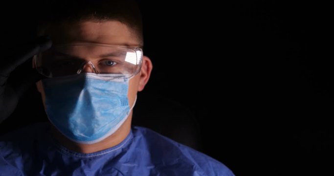 A lab worker in a mask puts on protective work glasses for working in laboratories. Concept of: Protective mask, Protective goggles, Safety precautions, Work gloves.