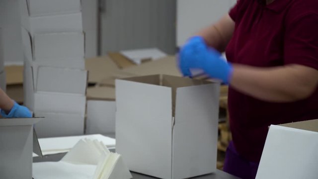 A factory female worker puts paper in the middle of an empty box and puts it on a conveyor