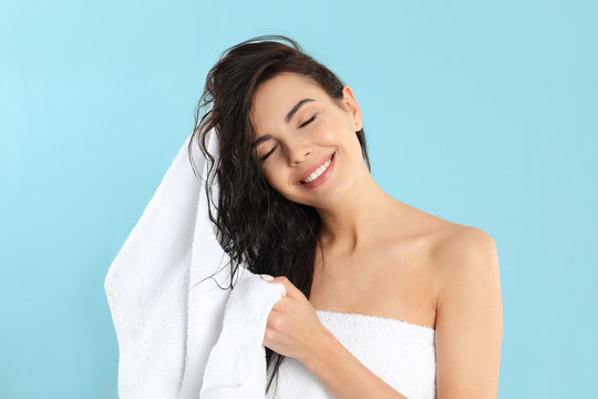 Young woman drying hair with towel on light blue background