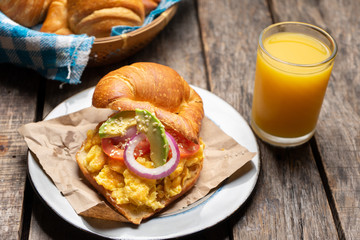 Butter croissant bread with scrambled eggs and avocado on wooden background