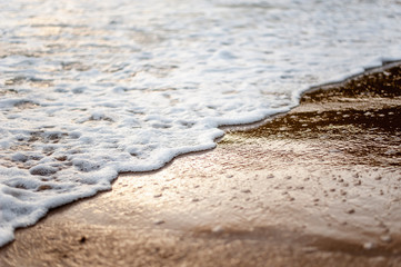 Fototapeta na wymiar Sea, beach, sand, wave, summer, background concept. White waves on a sandy beach in the summer on sunset. Background sea concept.
