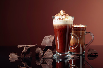 Hot chocolate with whipped cream and pieces of dark chocolate on a brown background.