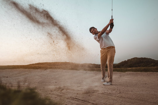 A man is sweeping golf on the sand with a beautiful posture at a golf course to practice golfing skills professionally at sunset in the summer. Sport lifestyle Concept.