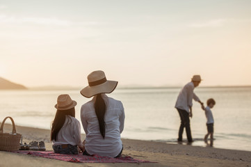 Fototapeta premium Family, travel, beach, relax, lifestyle, holiday concept. Parents and children who enjoy a picnic at the beach on sunset in holiday.