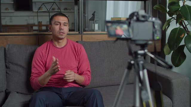 Handsome deaf-mute male web influnecer streaming live sign language vlog in domestic room. Hearing impaired blogger recording video for vlog on camera, talking using sign language indoors.