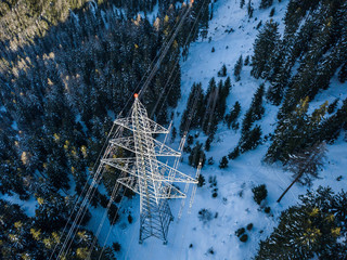Aerial view of power line pylon in alpine area in winter. Snow covered mountain and fir trees. Concept of power transmission.