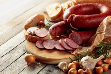 On a old wooden table sausage with bread, rosemary, onion and pepper.