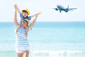Asian happy family have fun on the beach watching the landing planes. Traveling on an airplane for leisure and destination.  Mom and kid tourism travel in summer and holiday.  