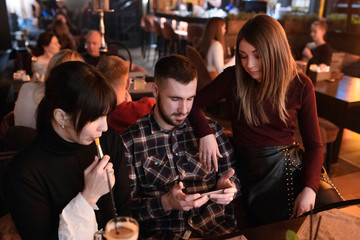 Friends at lounge bar looking at smartphone. two women and man in the restaurant at the dinner.