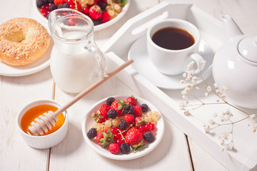 Fresh sweet berries on the white plate, bagel, cup of coffee and honey for breakfast.