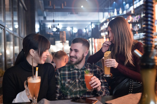 Young handsome hipster man flirting with two pretty girlfriends at the cocktail party in the lounge bar.