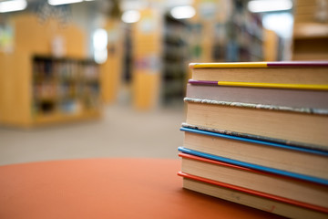 Neat stack of books on a round and brown wooden table in a library