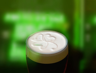 Famous black Irish stout with a frothy shamrock. Green St Patricks day background - obrazy, fototapety, plakaty