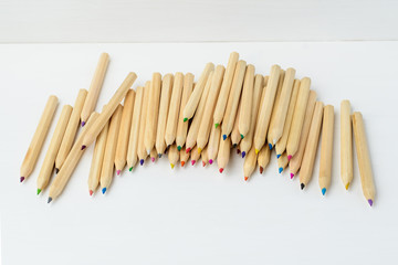 Line of many small wooden colored pencils displayed on a white painted table