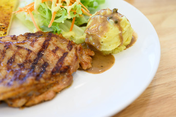 Selective focus grilled chicken steak set in white dish on wooden table background.Chicken grill, mashed potato, bread and salad.Restaurant menu.