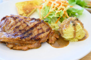 Selective focus grilled chicken steak set in white dish on wooden table background.Chicken grill, mashed potato, bread and salad.Restaurant menu.