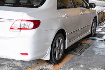 White car sedan on brake tester machine at garage. Selective focus at front car braking test.