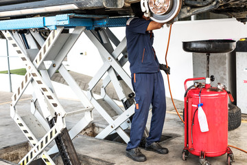 Auto mechanic in uniform standing under a lifted car to fix or repair. Car repair and maintenance.