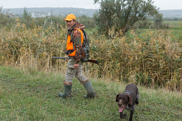 A man with a gun in his hands and an orange vest on a pheasant hunt in a wooded area in cloudy...