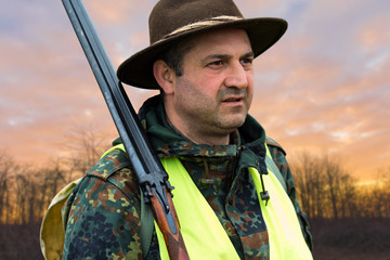 Silhouette of a hunter on the background of the morning red dawn. Stands at the ready with a gun.
