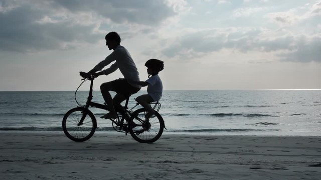 Asian family On Summer Vacation Father and son riding bicycles on beach Holiday and Travel concept. Silhouette Slow Motion