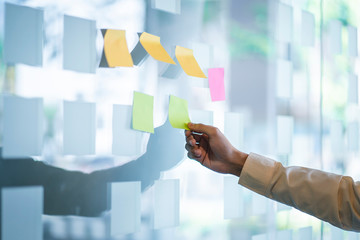 Businessman putting sticky note paper reminder on the glass wall.