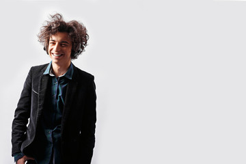 Handsome smiling ,funny guy, with curly awesome hair, in a jacket, listening to music, put headsome, isolated on a white background. Space for text.