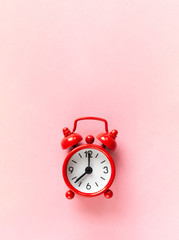 Red small alarm clock on pastel pink background with copy space, flat lay, macro. Minimalism style. Time management, countdown concept. Vertical orientation