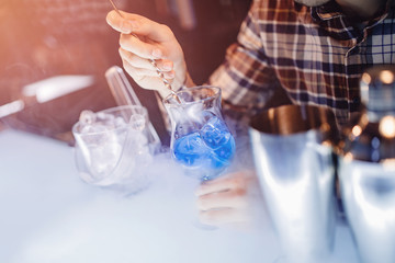 Fototapeta na wymiar Barman mixes blue cocktail show with colorful alcoholic and smoke bar counter