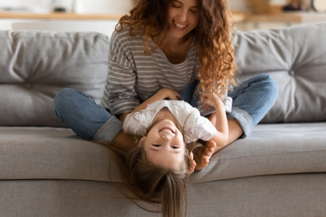 Funny mom playing with daughter seated on couch at home