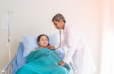 Senior male doctor using a stethoscope examining female patient on bed