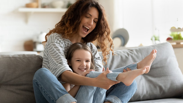 Mother playing with daughter seated on couch having fun indoors