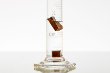 Density of 2 different materials in a graduated cylinder. One object floating and one sinking.