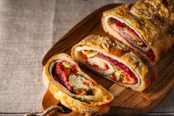 Traditional Italian Stromboli stuffed with cheese, salami, red pepper and spinach. Photo in a dark...