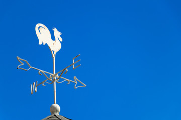 White rooster weather vane show the wind direction on blue sky background
