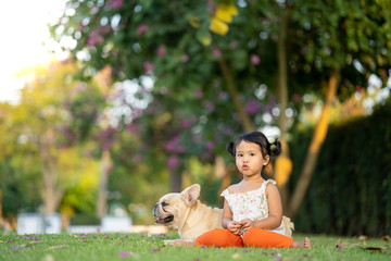 Cute little girl sitting with her french bulldog in park. 
