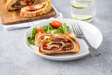Italian food Pizza roll stromboli with cheese, salami, spinach and red pepper a light background.