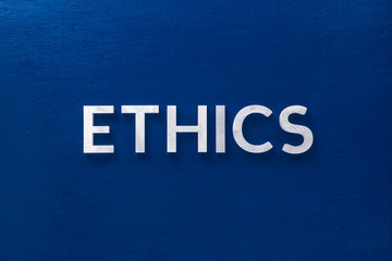 the word ethics laid with silver metal letters on classic blue board in flat lay with central...
