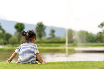 cute little girl sitting at park along the lake.