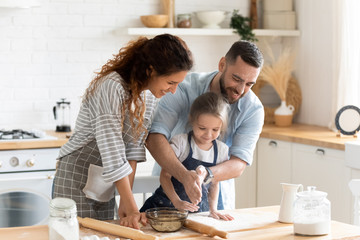Little kid girl preparing pie with parents on domestic kitchen