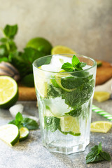 Summer cold drink and cocktail. Fresh Mojito cocktail with lime, ice and mint in a glass on a gray stone background. Copy space.