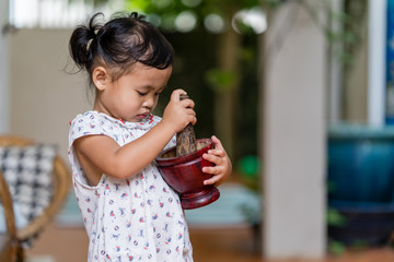 Cute little girl playing with wooden mortar and pestle indoor.