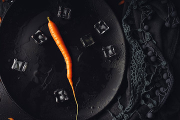 Fresh carrots on a black plate with ice. Food background for recipes and books